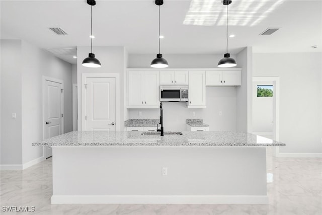 kitchen with white cabinets, sink, light stone countertops, and a kitchen island with sink