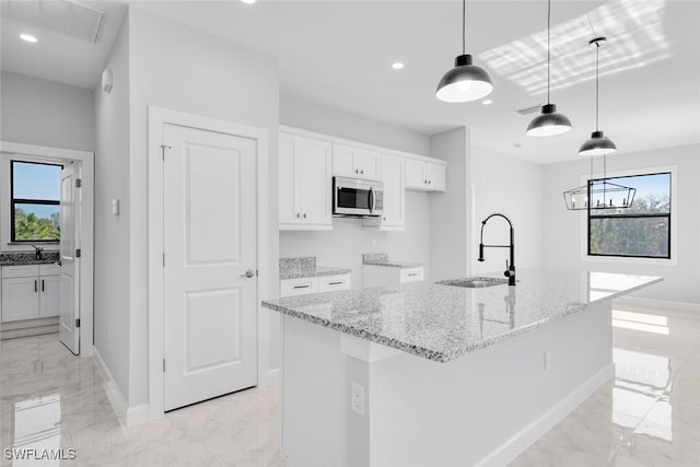 kitchen featuring a healthy amount of sunlight, a center island with sink, white cabinets, and pendant lighting