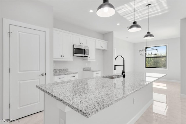 kitchen with pendant lighting, white cabinets, sink, an island with sink, and light stone counters