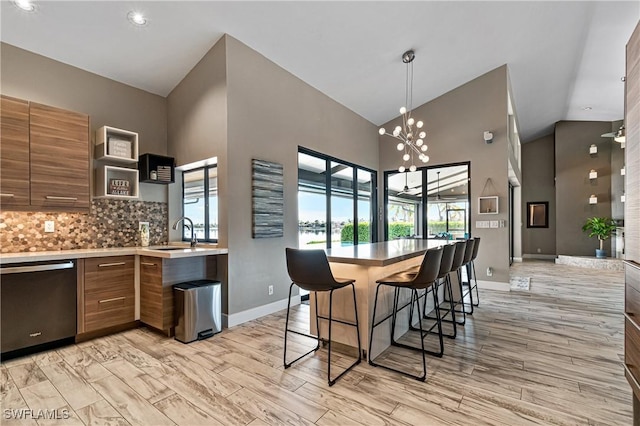 kitchen featuring stainless steel dishwasher, sink, decorative backsplash, a breakfast bar, and a chandelier