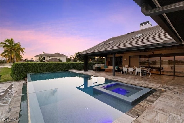 pool at dusk with an in ground hot tub, a patio area, and outdoor lounge area