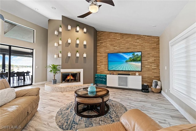 living room with a fireplace, light hardwood / wood-style flooring, high vaulted ceiling, and ceiling fan