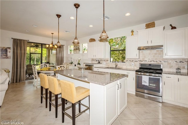 kitchen featuring visible vents, decorative light fixtures, light stone countertops, under cabinet range hood, and stainless steel range with gas cooktop