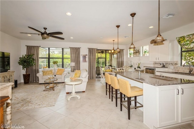 kitchen with pendant lighting, open floor plan, white cabinets, a sink, and dark stone counters