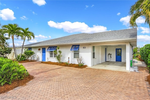 ranch-style home featuring stucco siding and roof with shingles