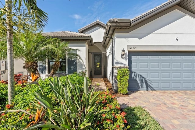 doorway to property with a garage, decorative driveway, and stucco siding