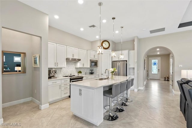 kitchen featuring under cabinet range hood, light countertops, appliances with stainless steel finishes, a center island with sink, and decorative light fixtures