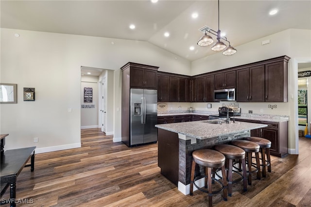 kitchen with a kitchen island with sink, hanging light fixtures, sink, appliances with stainless steel finishes, and light stone counters