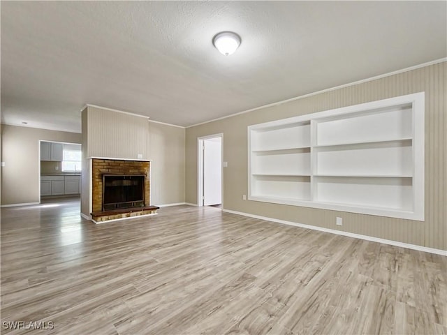 unfurnished living room with built in shelves, a brick fireplace, light hardwood / wood-style flooring, a textured ceiling, and ornamental molding