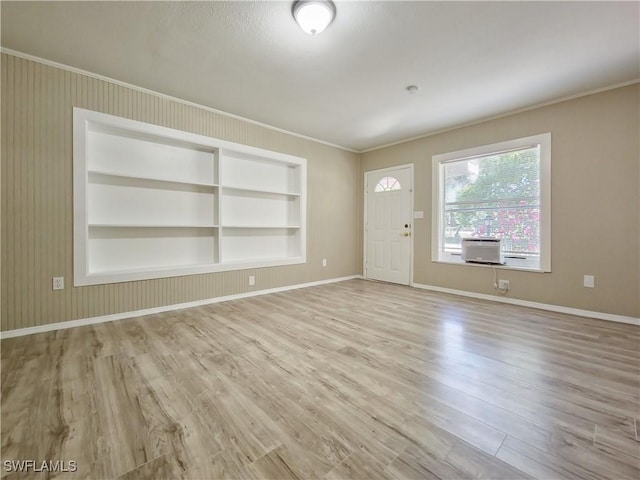 unfurnished room with built in shelves, light hardwood / wood-style floors, and ornamental molding