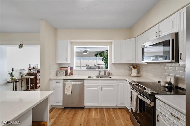 kitchen featuring white cabinets, stainless steel appliances, decorative backsplash, sink, and light hardwood / wood-style flooring