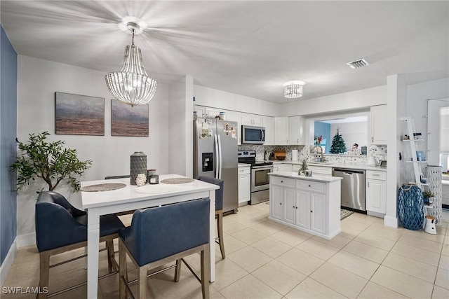 kitchen with appliances with stainless steel finishes, white cabinetry, tasteful backsplash, and decorative light fixtures