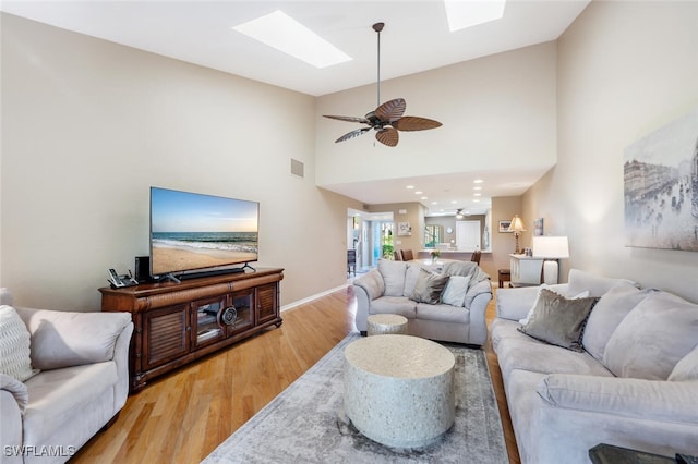 living room with a skylight, hardwood / wood-style floors, high vaulted ceiling, and ceiling fan