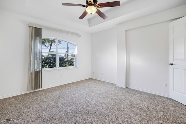 empty room with ceiling fan, a tray ceiling, and carpet