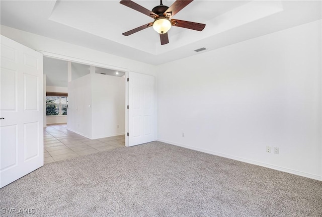 carpeted spare room with a raised ceiling and ceiling fan