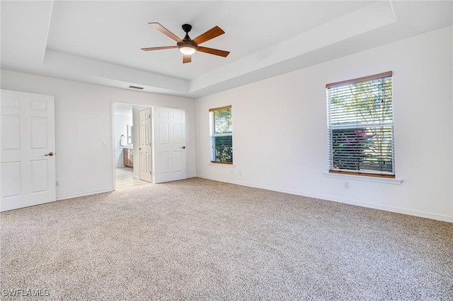 unfurnished bedroom featuring ceiling fan, multiple windows, connected bathroom, and a tray ceiling