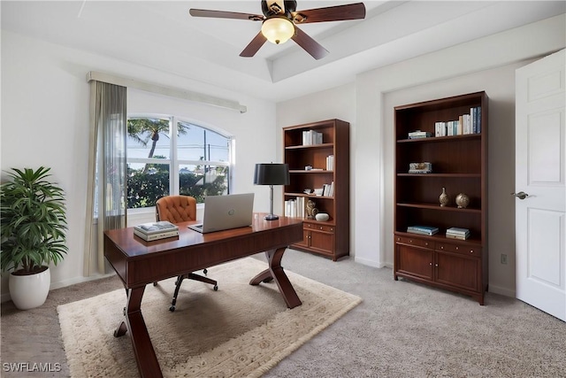 carpeted office space featuring ceiling fan and a tray ceiling