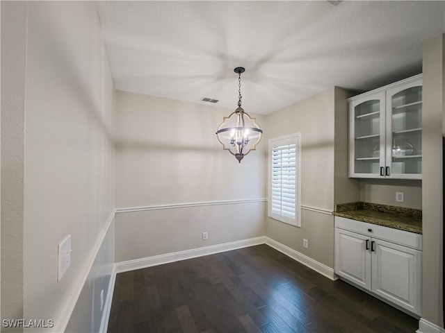 unfurnished dining area featuring a notable chandelier and dark hardwood / wood-style flooring