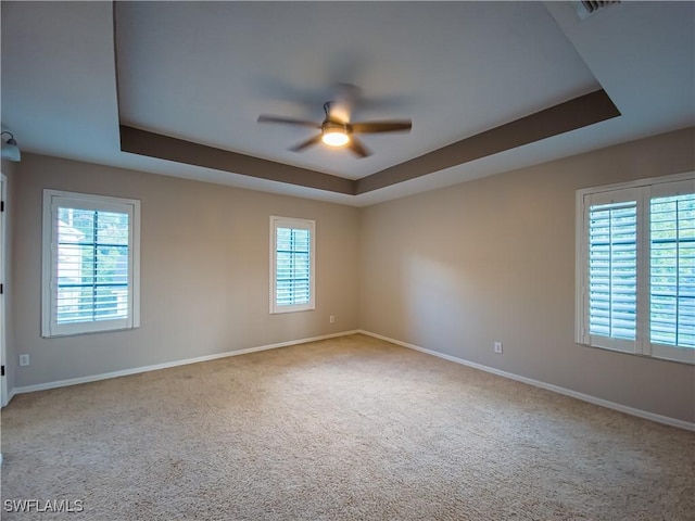 spare room featuring light colored carpet, a raised ceiling, ceiling fan, and a healthy amount of sunlight