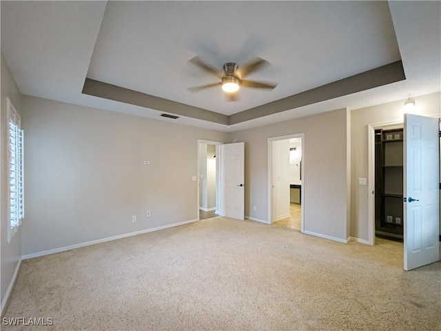 unfurnished bedroom with a raised ceiling, ceiling fan, a closet, and light colored carpet