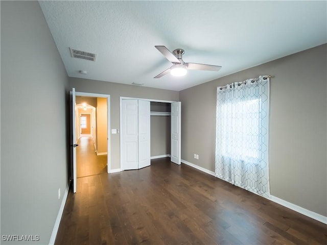 unfurnished bedroom with a textured ceiling, dark hardwood / wood-style flooring, a closet, and ceiling fan