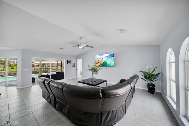 tiled living room featuring lofted ceiling, visible vents, a ceiling fan, and baseboards