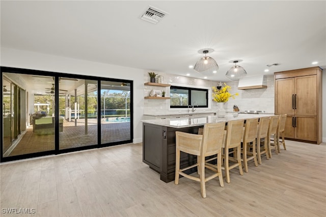 kitchen featuring tasteful backsplash, light hardwood / wood-style floors, a spacious island, and custom exhaust hood