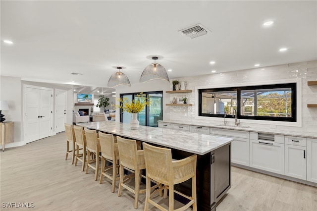 kitchen with a center island, sink, light stone counters, a breakfast bar, and white cabinets