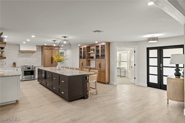 kitchen with a center island, light stone counters, premium range hood, decorative backsplash, and stainless steel stove