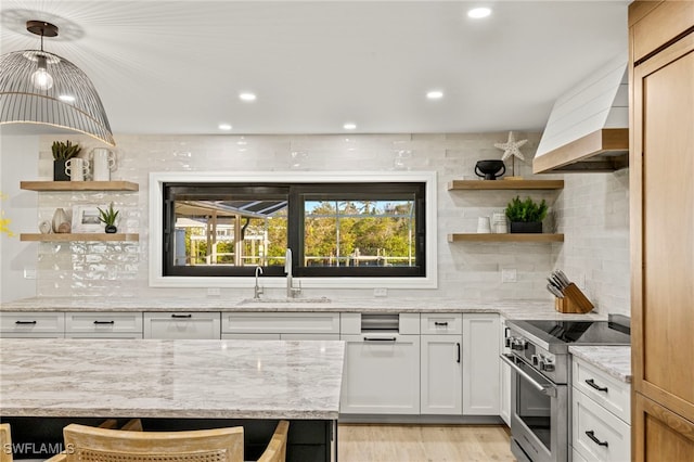 interior space featuring sink, light stone countertops, high end stove, decorative light fixtures, and white cabinetry