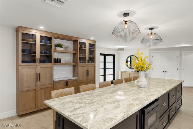 kitchen with stainless steel microwave, a center island, light stone counters, decorative light fixtures, and light wood-type flooring