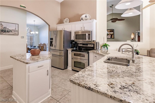 kitchen featuring light stone counters, stainless steel appliances, white cabinetry, a sink, and ceiling fan with notable chandelier