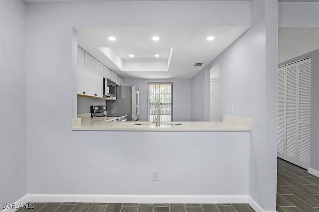 kitchen featuring sink, stainless steel appliances, a tray ceiling, white cabinets, and kitchen peninsula