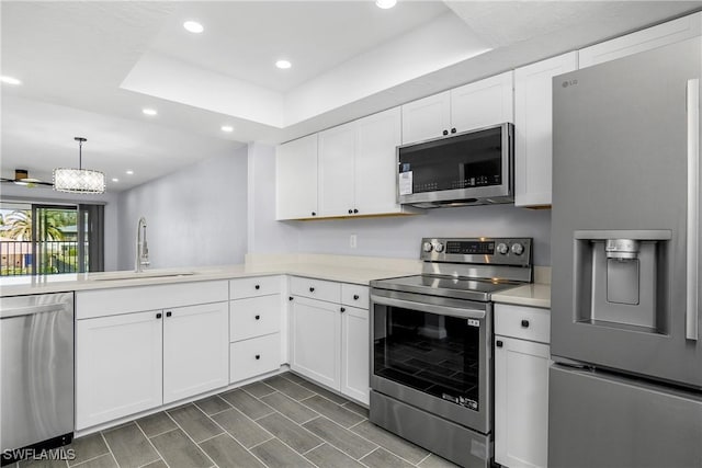 kitchen with appliances with stainless steel finishes, pendant lighting, sink, white cabinets, and a tray ceiling