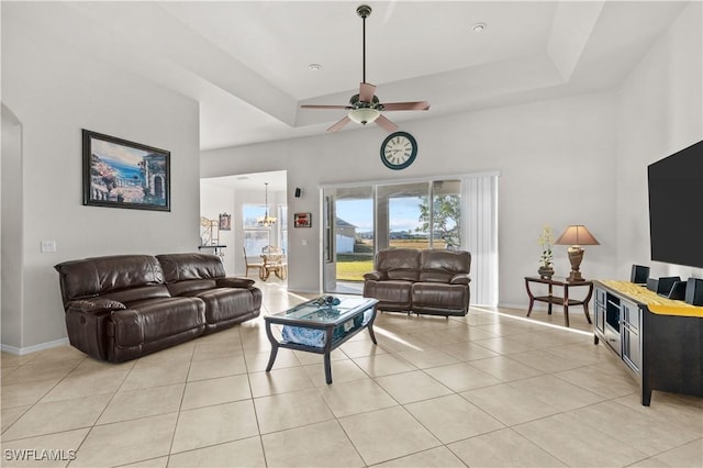 tiled living room featuring ceiling fan with notable chandelier and a tray ceiling