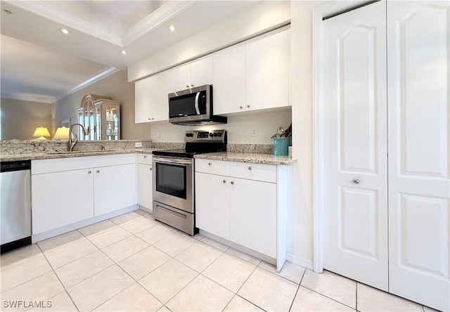 kitchen with appliances with stainless steel finishes, ornamental molding, sink, light tile patterned floors, and white cabinetry