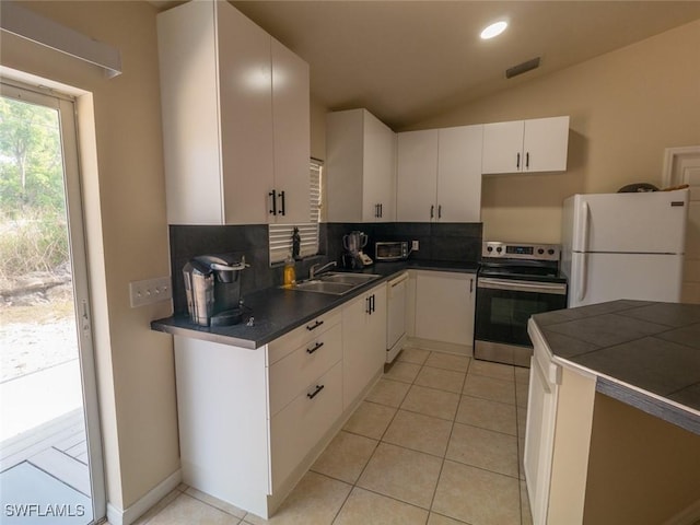 kitchen with lofted ceiling, white appliances, sink, light tile patterned floors, and white cabinetry