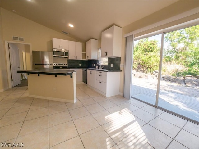 kitchen with a center island, stainless steel appliances, white cabinets, vaulted ceiling, and light tile patterned flooring