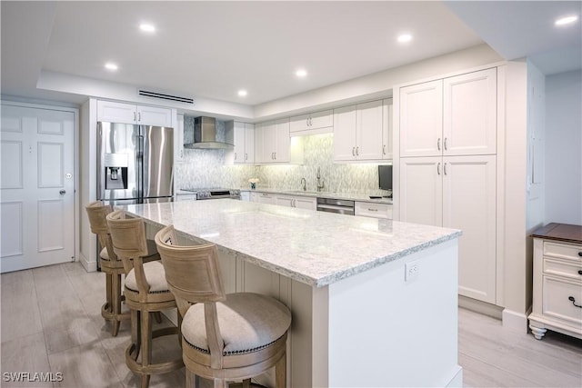 kitchen featuring white cabinets, a center island, wall chimney range hood, and appliances with stainless steel finishes