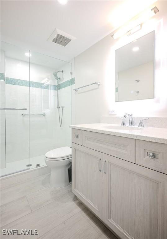 bathroom featuring vanity, a shower with shower door, and toilet