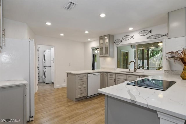 kitchen with gray cabinetry, sink, kitchen peninsula, white appliances, and stacked washer and clothes dryer