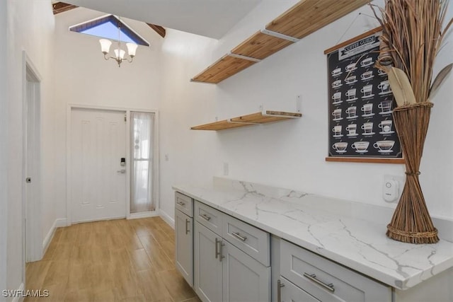 kitchen with gray cabinetry, light stone counters, lofted ceiling, and light hardwood / wood-style flooring