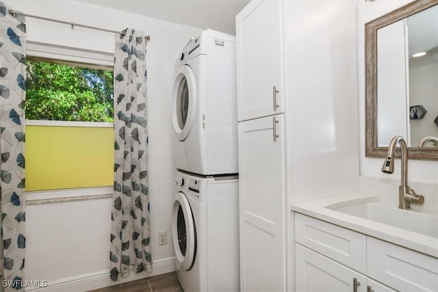 laundry room featuring cabinets, stacked washing maching and dryer, and sink