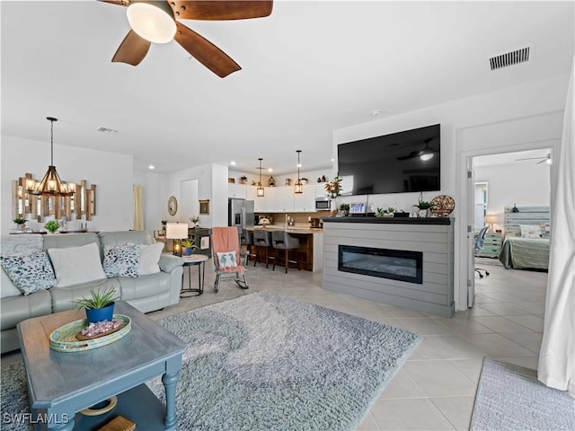 tiled living room with ceiling fan with notable chandelier