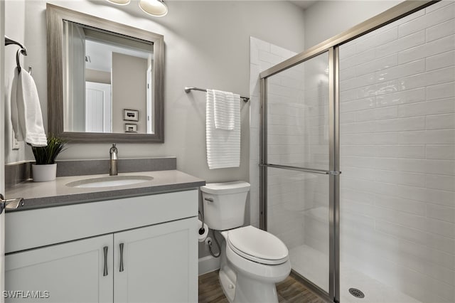 bathroom with wood-type flooring, vanity, toilet, and a shower with shower door