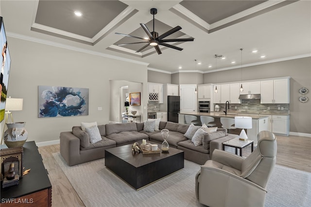 living room featuring light wood-type flooring, ornamental molding, coffered ceiling, ceiling fan, and sink