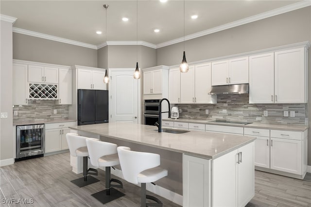 kitchen with a center island with sink, white cabinetry, beverage cooler, and sink