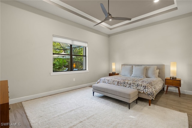 bedroom featuring a tray ceiling, ceiling fan, crown molding, and wood-type flooring