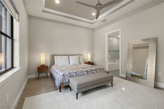 bedroom with hardwood / wood-style floors, ensuite bathroom, a raised ceiling, and ceiling fan