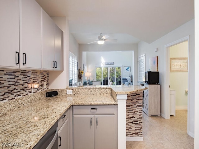 kitchen featuring light tile patterned flooring, light stone counters, kitchen peninsula, ceiling fan, and backsplash